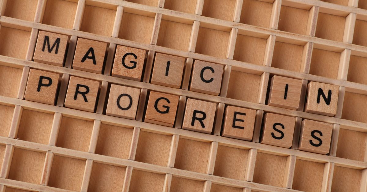 Wooden letter blocks arranged to spell 'Magic in Progress' on a grid.